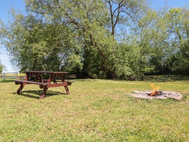 A picnic table and a small fire pit on grass with trees in the background at Granary 2 in Madley