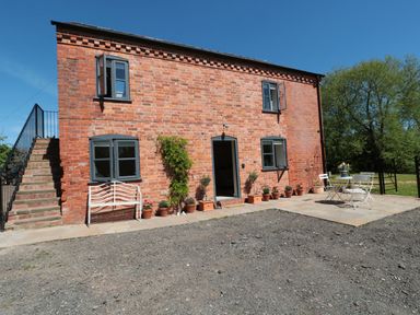 A brick two-story house with gray windows and door surrounded by potted plants and outdoor seating at Granary 2 in Madley