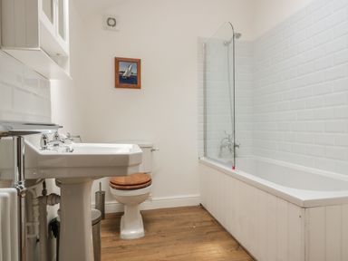 A bathroom with a sink toilet with wooden seat and a bathtub with glass shower screen at Granary 2 in Madley