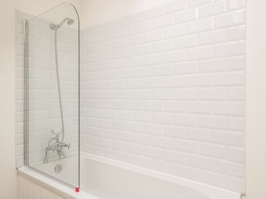 A bathroom with a bathtub shower and white tiled walls at Granary 2 in Madley