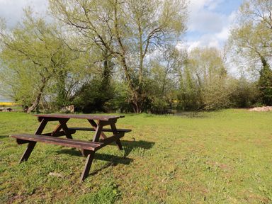 A wooden picnic table on grass with trees and a small pond in the background at Granary 1 Madley near Hereford