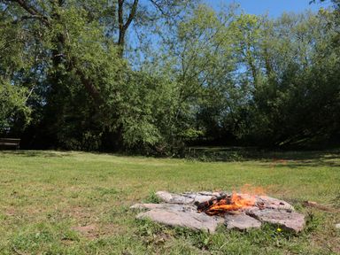 An outdoor scene with a fire pit made of stones burning wood on grass near trees at Granary 1 Madley near Hereford