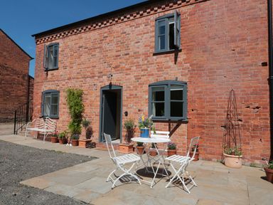 A brick house with blue framed windows and a door with outdoor white table and chairs and potted plants on a patio at Granary 1 in Madley near Hereford