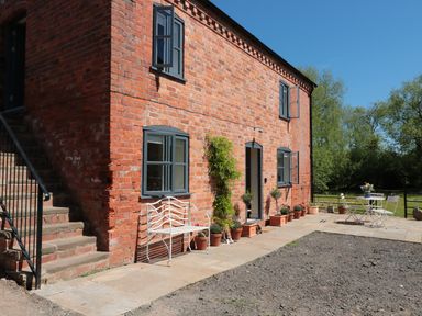 An exterior view of a red brick building with blue-grey windows and doors with potted plants a white bench and a white table with chairs on a patio at Granary 1 Madley near Hereford