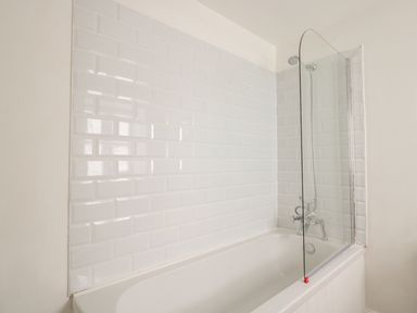 A bathtub with white subway tiles on the wall and a glass shower screen at Granary 1 in Madley near Hereford