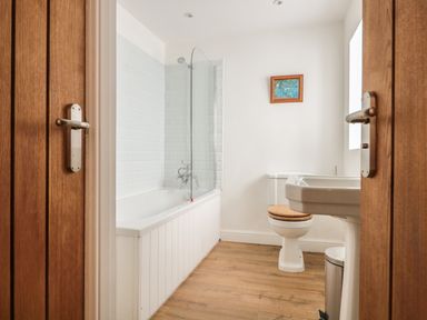 A bathroom with a bathtub with glass shower screen a toilet with wooden seat a pedestal sink and wooden doors at Granary 1 Madley near Hereford