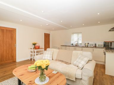 An open plan living room and kitchen with a beige sofa and wooden coffee table at Granary 1 in Madley near Hereford