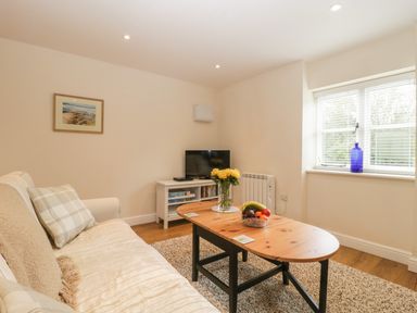 A living room with a sofa a wooden coffee table with flowers and fruit a tv on a white stand and a window with blinds at Granary 1 Madley near Hereford