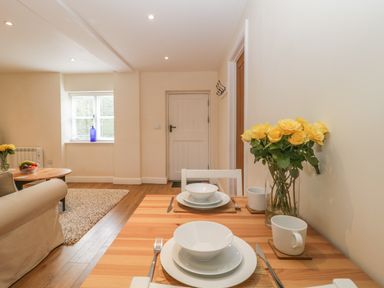 A dining table set with dishes and yellow flowers beside a living room with a window and wooden floor at Granary 1 in Madley near Hereford