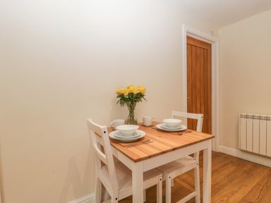 A small dining table with two chairs set with white bowls plates mugs and a vase of yellow flowers at Granary 1 Madley near Hereford