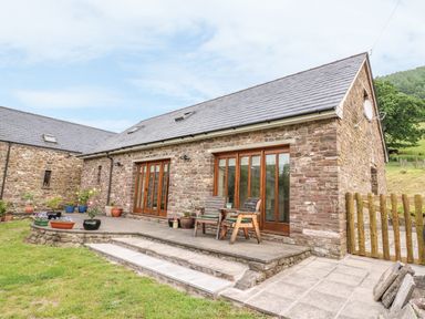An outdoor stone patio with potted plants and two wooden chairs outside a stone house at The Barn in Abergavenny