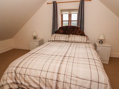 A bedroom with a double bed between two bedside tables with lamps and a window behind the bed at The Barn in Abergavenny