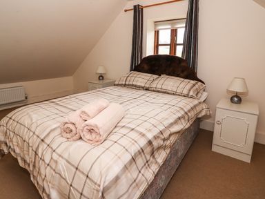 A bedroom with a double bed with plaid bedding and rolled towels on top two nightstands with lamps and a small window with curtains at The Barn in Abergavenny