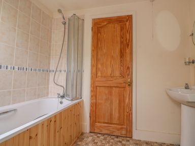 A bathroom with a bathtub shower combination wooden door and a pedestal sink at The Barn in Abergavenny