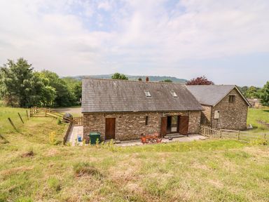 A stone house with a slate roof and patio furniture outside in a rural area at The Barn in Abergavenny
