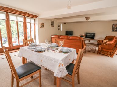 A dining table set with plates and glasses and wooden chairs next to a living area with leather sofas and a television at The Barn in Abergavenny