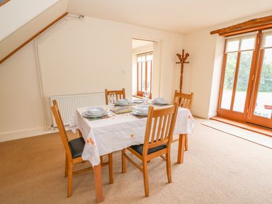A dining area with a table set for four and wooden chairs next to glass doors at The Barn in Abergavenny