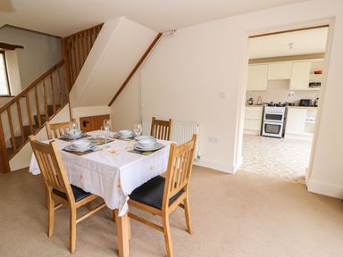 A dining area with a table set for four and wooden chairs next to a staircase and an open doorway leading to a kitchen at The Barn in Abergavenny