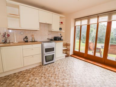 A kitchen with white cabinets a stove and large wooden framed windows showing an outdoor bench at The Barn in Abergavenny
