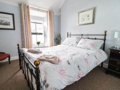 A bedroom with a double bed with bird and flower patterned bedding near a window with curtains at Preswylfa in Penmachno