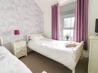 A bedroom with two single beds a nightstand with a lamp purple curtains and a window at Preswylfa in Penmachno