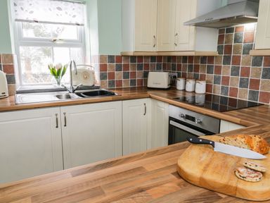 A kitchen with wooden countertops cutting board with bread and knife tiled backsplash and window at Preswylfa in Penmachno