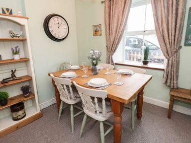 A dining room with a wooden table set for six and a wall clock at Preswylfa in Penmachno