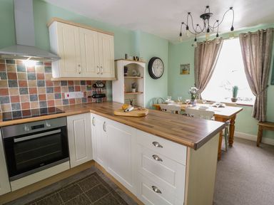 A kitchen with wooden countertops white cabinets a dining table with chairs and a large window with curtains at Preswylfa in Penmachno
