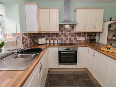 A kitchen with wooden countertops white cabinets a stainless steel oven a sink a toaster and a cutting board with bread at Preswylfa in Penmachno