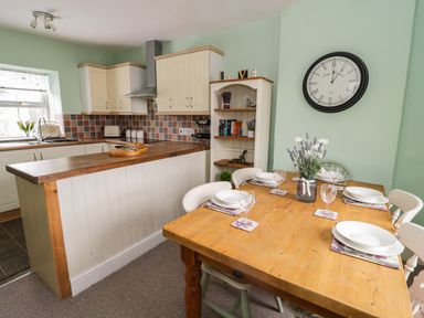 A kitchen with cream cabinets and a wooden countertop next to a dining table set for four with plates and glasses at Preswylfa in Penmachno
