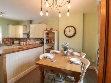A kitchen and dining area with a wooden table set for four chairs and shelves with decorations at Preswylfa Penmachno
