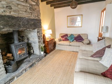 A living room with two sofas a wood burning stove a rug and side tables at Preswylfa in Penmachno
