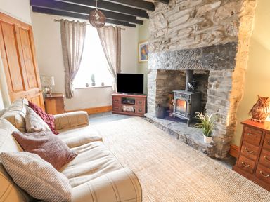 A living room with a plaid sofa cushions window with curtains stone fireplace wood stove television on wooden stand and wooden furniture at Preswylfa in Penmachno