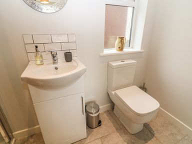 A bathroom with a sink cabinet, a toilet, a trash can, and a window with a jug on the sill at Cae Glas in Pwllheli