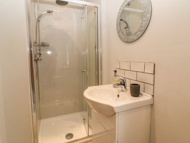 A bathroom with a glass shower enclosure a white sink with soap dispenser and a round mirror at Cae Glas in Pwllheli