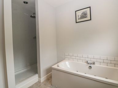 A bathroom with a bathtub and a shower area with a framed picture on the wall at Cae Glas in Pwllheli
