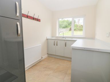 A kitchen with grey cabinets a sink a window and a coat rack at Cae Glas in Pwllheli