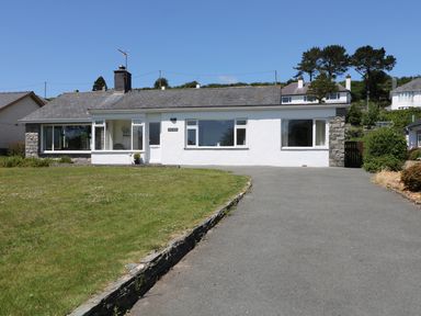A single-story house with white walls and stone details viewed from the driveway at Cae Glas in Pwllheli