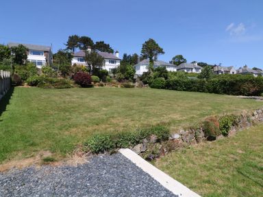 A grassy garden area with stone edging shrubs and houses in the background at Cae Glas in Pwllheli