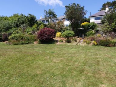 A grassy garden area with shrubs and houses in the background at Cae Glas in Pwllheli