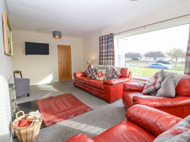 A living room with red leather sofas a red rug a basket a wall-mounted tv and large windows at Cae Glas in Pwllheli