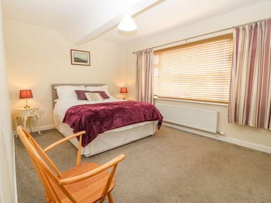 A bedroom with a double bed two bedside tables with lamps a wooden chair and a large window with blinds and curtains at Cae Glas in Pwllheli