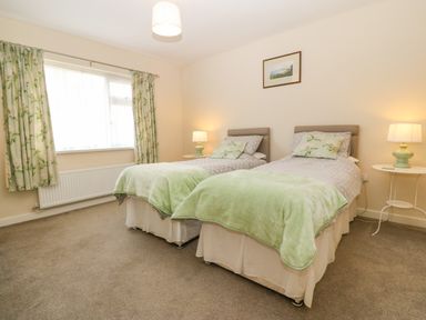 A bedroom with two single beds green blankets and floral curtains at Cae Glas in Pwllheli