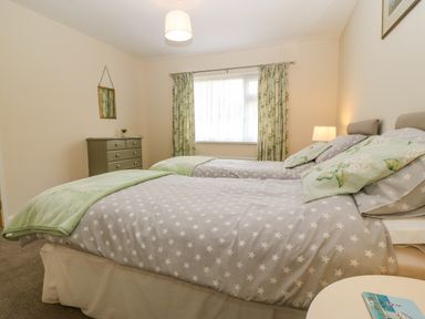 A bedroom with two single beds a chest of drawers and a window with curtains at Cae Glas in Pwllheli