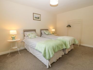 A bedroom with two single beds lamps on round white side tables and a clothes rack at Cae Glas Pwllheli