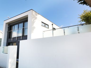 A modern two-story house with large windows and glass balcony railings at An Drowes in Newquay