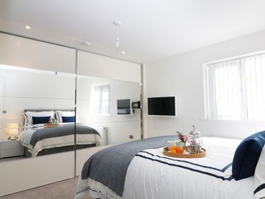 A bedroom with a bed a tray with breakfast a wall mounted television and mirrored wardrobes at An Drowes in Newquay