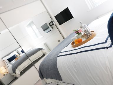 A bedroom with a bed having a tray with fruit and cups a wall mounted TV and mirrored closet doors at An Drowes in Newquay