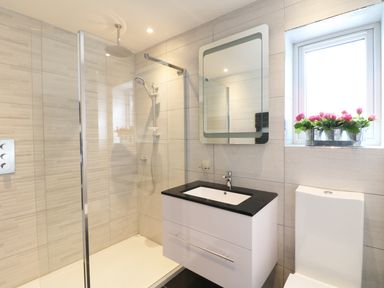 A bathroom with a walk-in shower a sink with black countertop a toilet and flowers on a window sill at An Drowes in Newquay