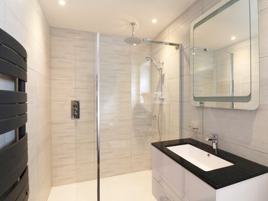 A bathroom with a walk in shower a black countertop sink and a mirror at An Drowes in Newquay